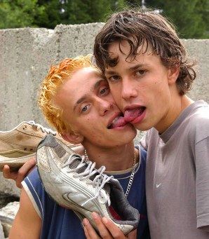 A bleached strawberry blond and a brunet holding their dirty sneakers and swapping spit