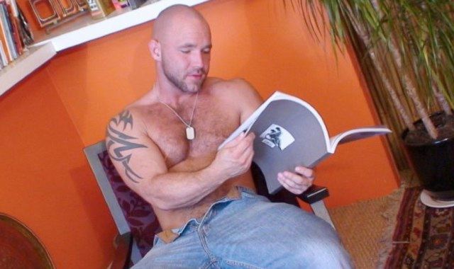 Beefy hairy man reads a book shirtless
