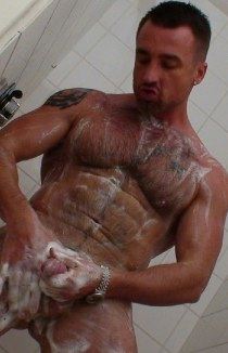 Tanned muscle guy soaps up his rod in the shower