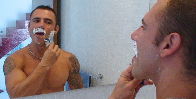 Pedro Adreas looks at himself in a mirror as he shaves