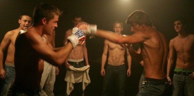Two hot guys boxing in a dark room surrounded by hot young shirtless guys