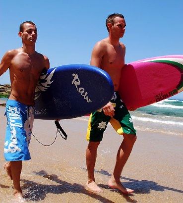 Two hot surfers on the beach with their boards