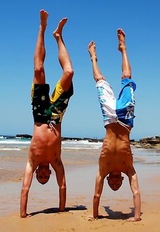 Two guys on the beach doing hand stands