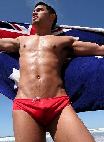 Tanned Eurasian swimmer in red trunks with Australian flag towel