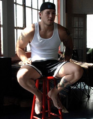 Built jock with tattooes sitting in shorts and tank top
