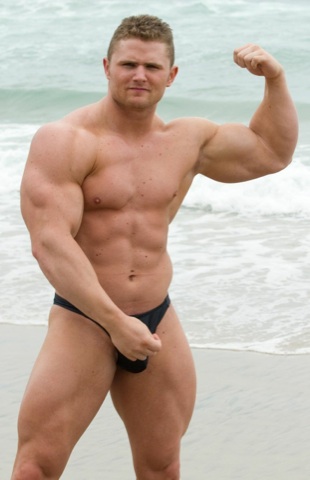 Rusty Winchester posing on the beach in a speedo