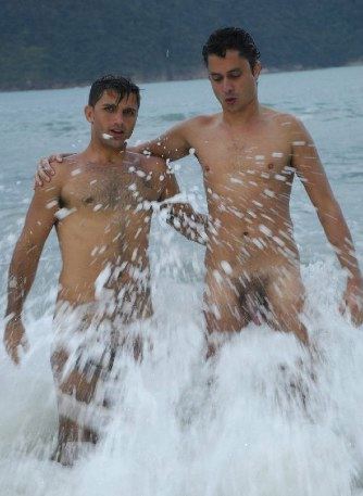 Two naked guys play in the surf