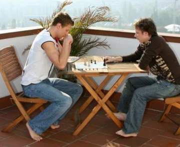 Two young guys playing chess on a veranda